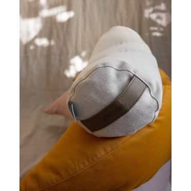 Mały wałek gryczany WellB w kolorze piaskowym leży na dużym wałku w odcieniu musztardowym, w tle jasna zasłona i światło cieni drzew.